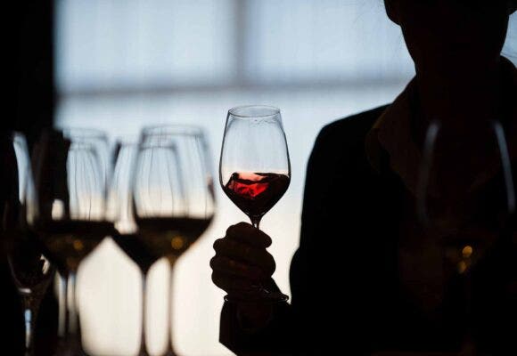 Silhouetted person swirls red wine in glass