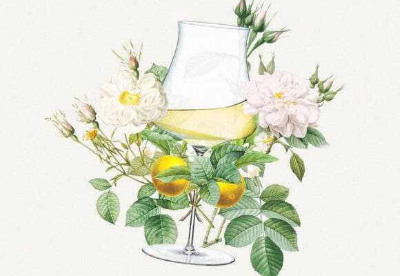 A glass of white wine surrounded by lavish flowers and citrus fruits