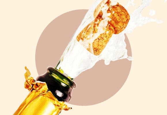 Close up of a champagne bottle popping on a tan background