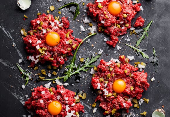 Beef tartare with pickled cucumber and fresh onion on dark marble background