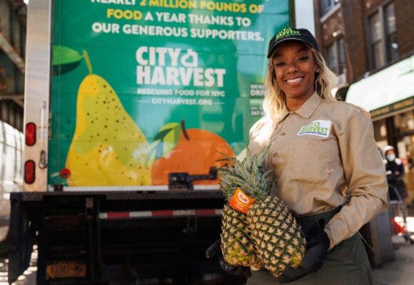City Harvest member holding pineapple in front of City Harvest delivery truck.